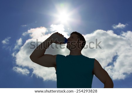 Smiling young man drinking water against blue sky with clouds and sun