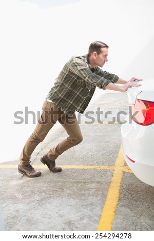 Man pushing his broken down car in a car park