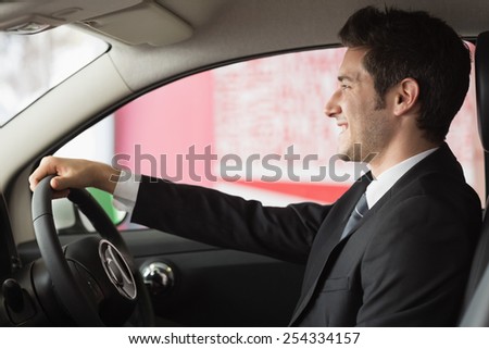 Smiling businessman at the wheel sitting in a car for sale at new car showroom