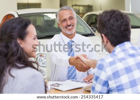 Smiling salesman shaking a customer hand at new car showroom
