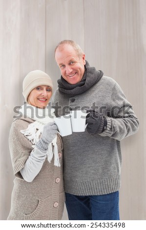 Happy mature couple in winter clothes holding mugs against bleached wooden planks background