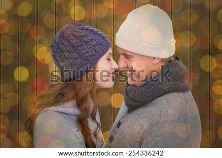 Couple in warm clothing facing each other against close up of christmas lights