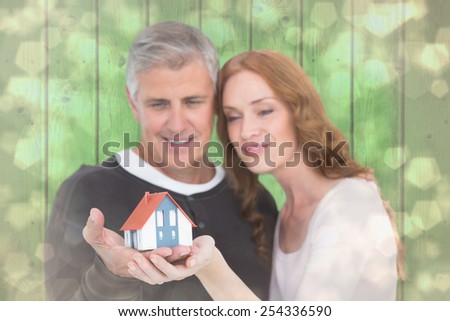 Casual couple holding small house against light glowing dots design pattern