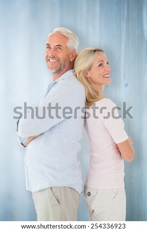 Smiling couple standing leaning backs together against bleached wooden planks background