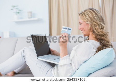 Happy blonde sitting on couch shopping online at home in the living room