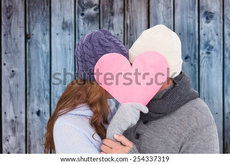 Couple in warm clothing holding heart against wooden background in blue