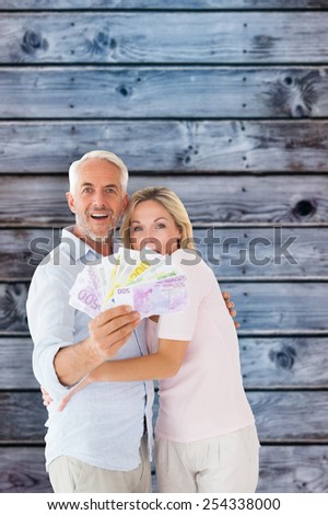 Happy couple flashing their cash against wooden background in blue