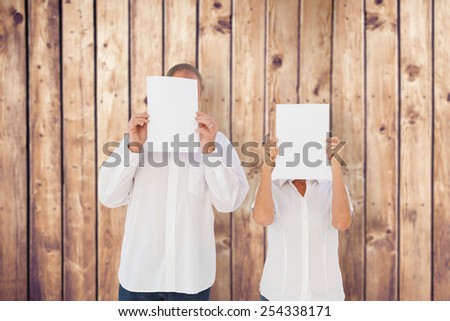 Couple holding paper over their faces against wooden planks