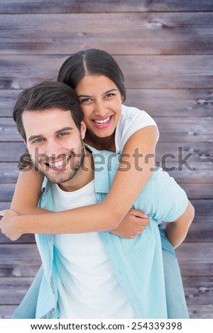 Happy casual man giving pretty girlfriend piggy back against faded grey wooden planks