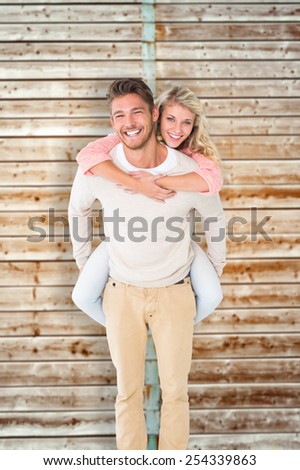 Handsome man giving piggy back to his girlfriend against wooden background in pale wood