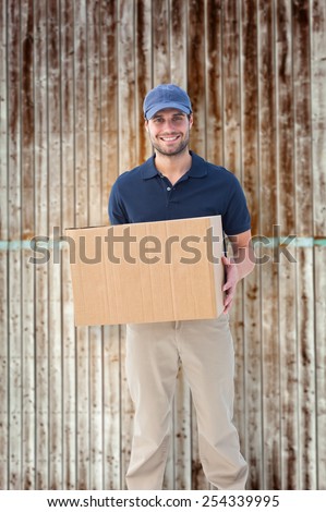 Happy delivery man holding cardboard box against wooden planks