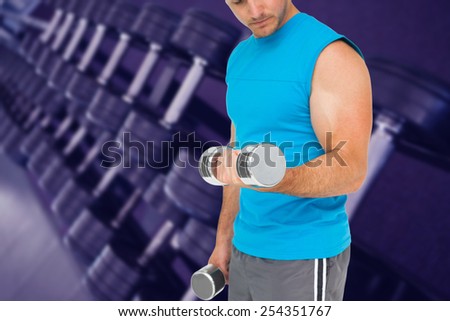 Mid section of a fit man exercising with dumbbells against heavy black dumbbells on rack in weights room