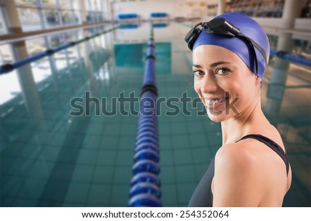 Fit swimmer standing by the pool smiling at camera against empty swimming pool with lane markers