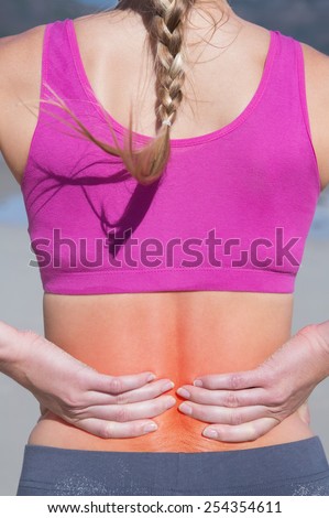Fit woman touching her sore back on the beach on a sunny day
