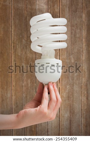 Hand holding energy efficient light bulb against wooden planks background