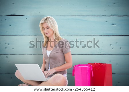 Happy blonde shopping online with laptop against painted blue wooden planks