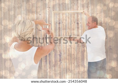Mature couple hanging up picture frame against light glowing dots design pattern