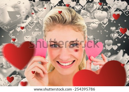Attractive young blonde holding little hearts against grey valentines heart pattern