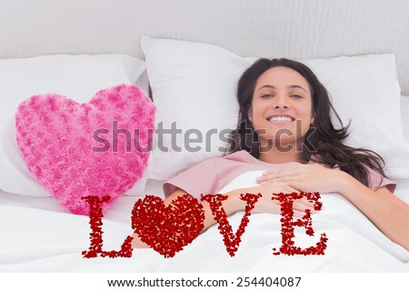 Woman lying in her bed next to a pink heart pillow against love spelled out in petals