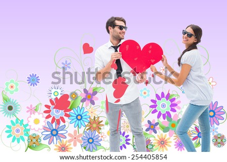 Hipster couple smiling at camera holding a heart against digitally generated girly floral design