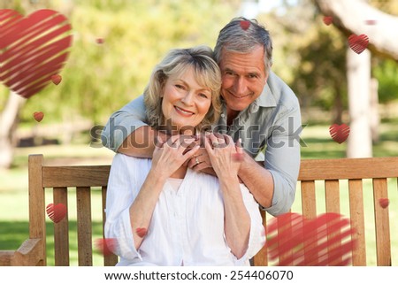 Elderly man hugging his wife who is on the bench against hearts