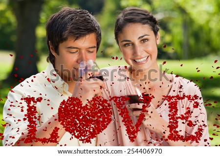 Woman smiling while her friend is drinking wine against love spelled out in petals