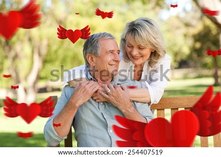 Senior woman hugging her husband who is on the bench against hearts
