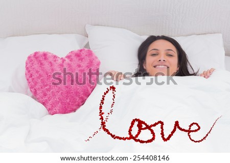 Woman lying in bed next to a fluffy heart pillow against love spelled out in petals