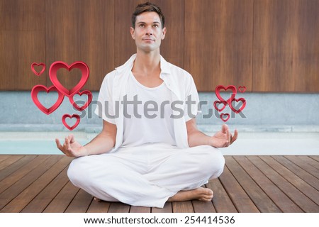 Handsome man in white meditating in lotus pose against pink hearts