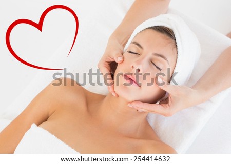 Attractive woman receiving facial massage at spa center against heart
