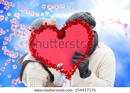 Attractive young couple in warm clothes holding red heart against digitally generated pretty flower background