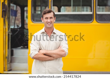 Smiling bus driver standing with arms crossed in front of his bus