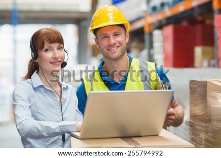 Smiling businesswoman wearing headset using laptop in warehouse