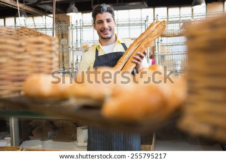 Cheerful waiter holding two baguettes at the bakery