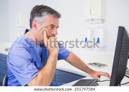 Serious dentist sitting and using computer in dental clinic