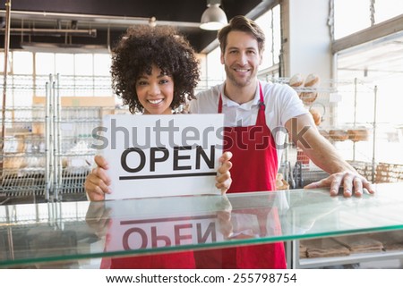Smiling co-workers showing open sign at the bakery