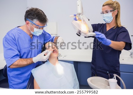 Dentist doing injection to his patient and nurse adjusting the light in dental clinic
