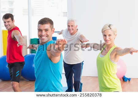 Portrait of happy men and women doing warrior pose in yoga class