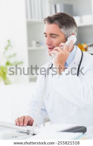 Male doctor using computer while on call at table in clinic