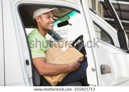 Smiling delivery driver in his van holding parcel outside warehouse