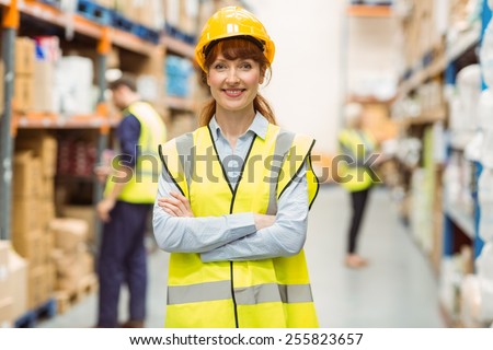 Warehouse manager smiling at camera with arms crossed in a large warehouse