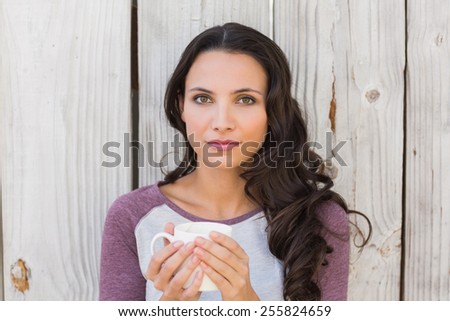 Pretty brunette holding a mug against bleached wooden fence