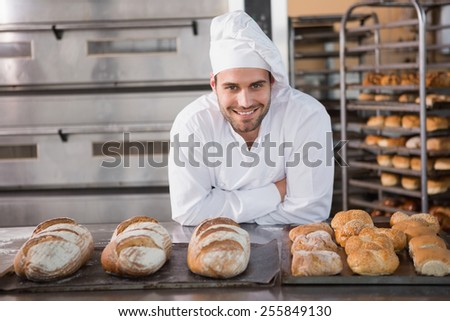 Happy baker standing near tray with bread at the bakery