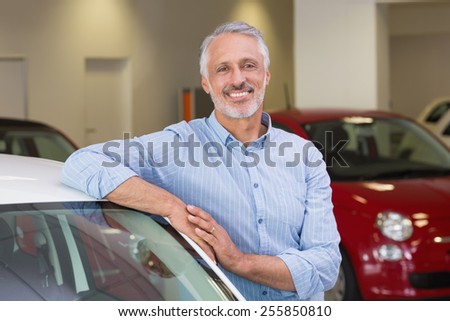 Smiling customer leaning on car at new car showroom