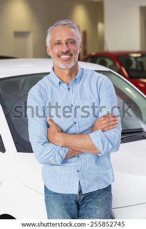 Smiling customer leaning on car with arms crossed at new car showroom