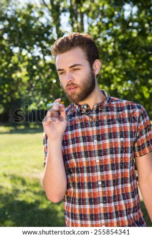 Hipster smoking an electronic cigarette on a summers day