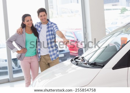 Smiling couple pointing a car at new car showroom