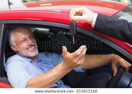 Smiling man driving a car while salesman his giving key at new car showroom
