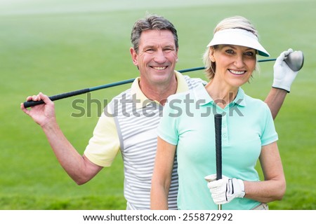 Golfing couple smiling at camera holding clubs on a foggy day at the golf course