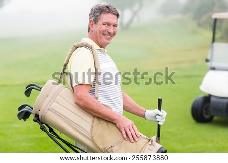 Happy golfer with golf buggy behind on a foggy day at the golf course
